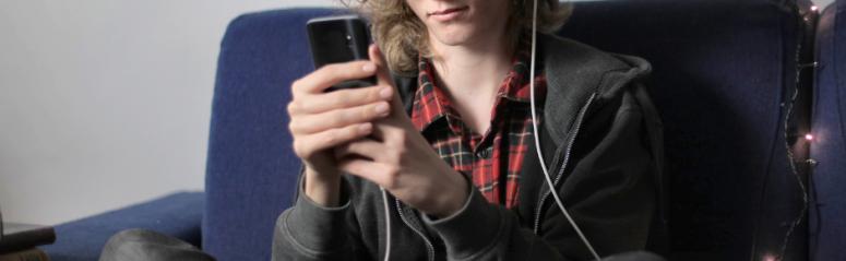 A teenager sits with his headphones in looking at his phone