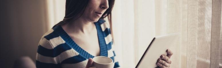A lady looks at a tablet computer and holds a cup of tea