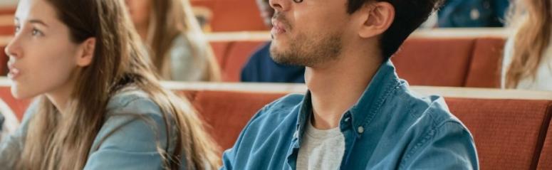 A man sits in a lecture theatre watching a presentation